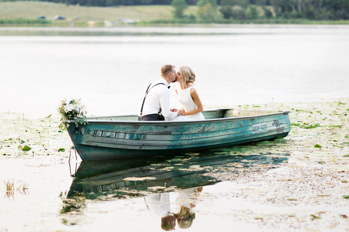 Bride and groom riding in a boat, kissing at a beautiful romantic sunset, creating a timeless intimate moment at Detroit Lake in Minnesota, captured by Toly Dzyuba Photography.