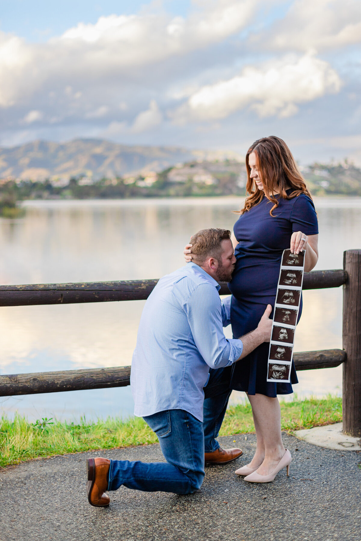 dad kisses moms belly as she holds sonogram