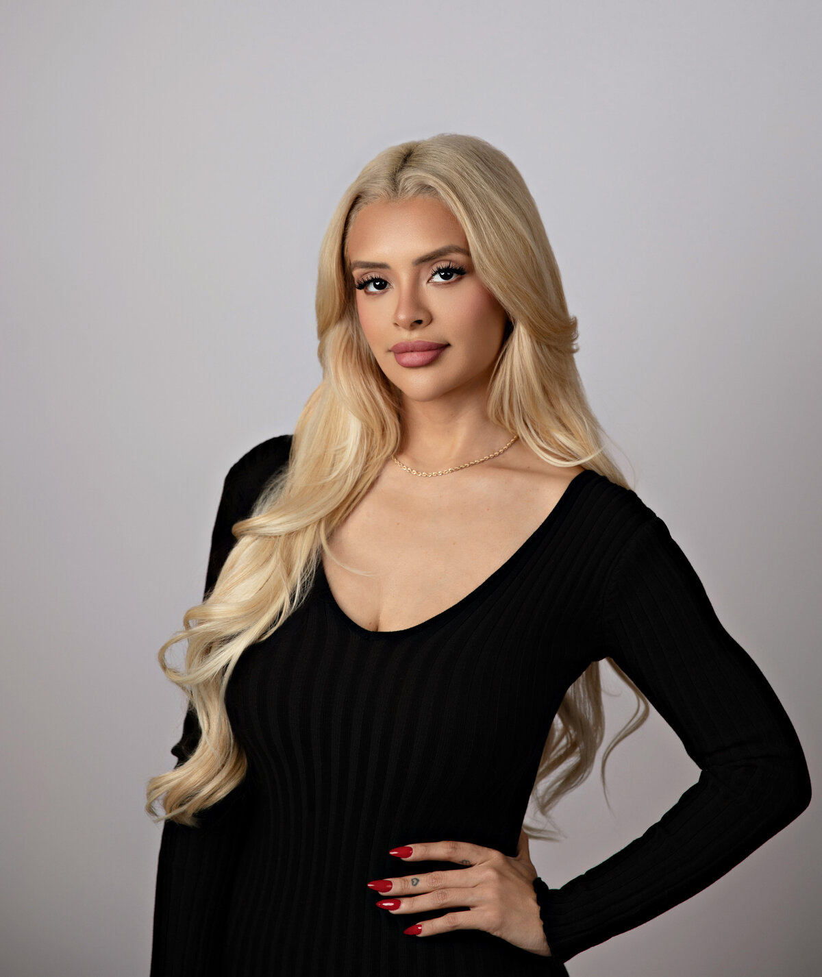 Woman with long blonde hair wearing a fitted black dress, hand on hip, posing confidently in a studio—Eva Magaña Photography, San Antonio.