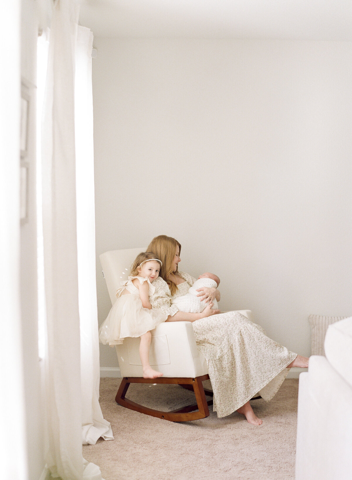 Toddler hangs off the side of a rocker while mom holds her baby brother. Image by Raleigh newborn photographer A.J. Dunlap Photography.
