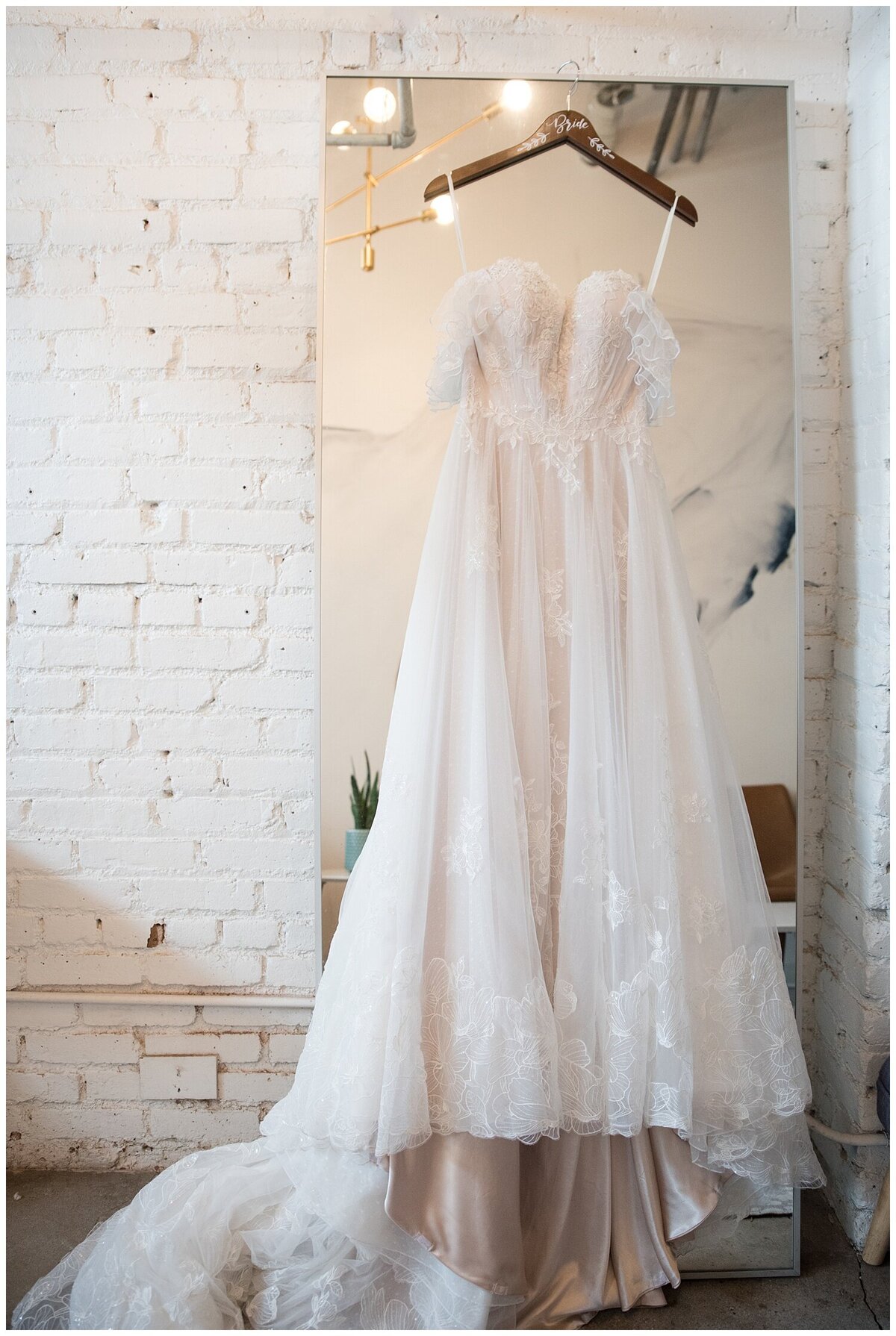 A white wedding dress hanging on a mirror with a white brick behind the mirror in the bridal suite at Skylight in Dener