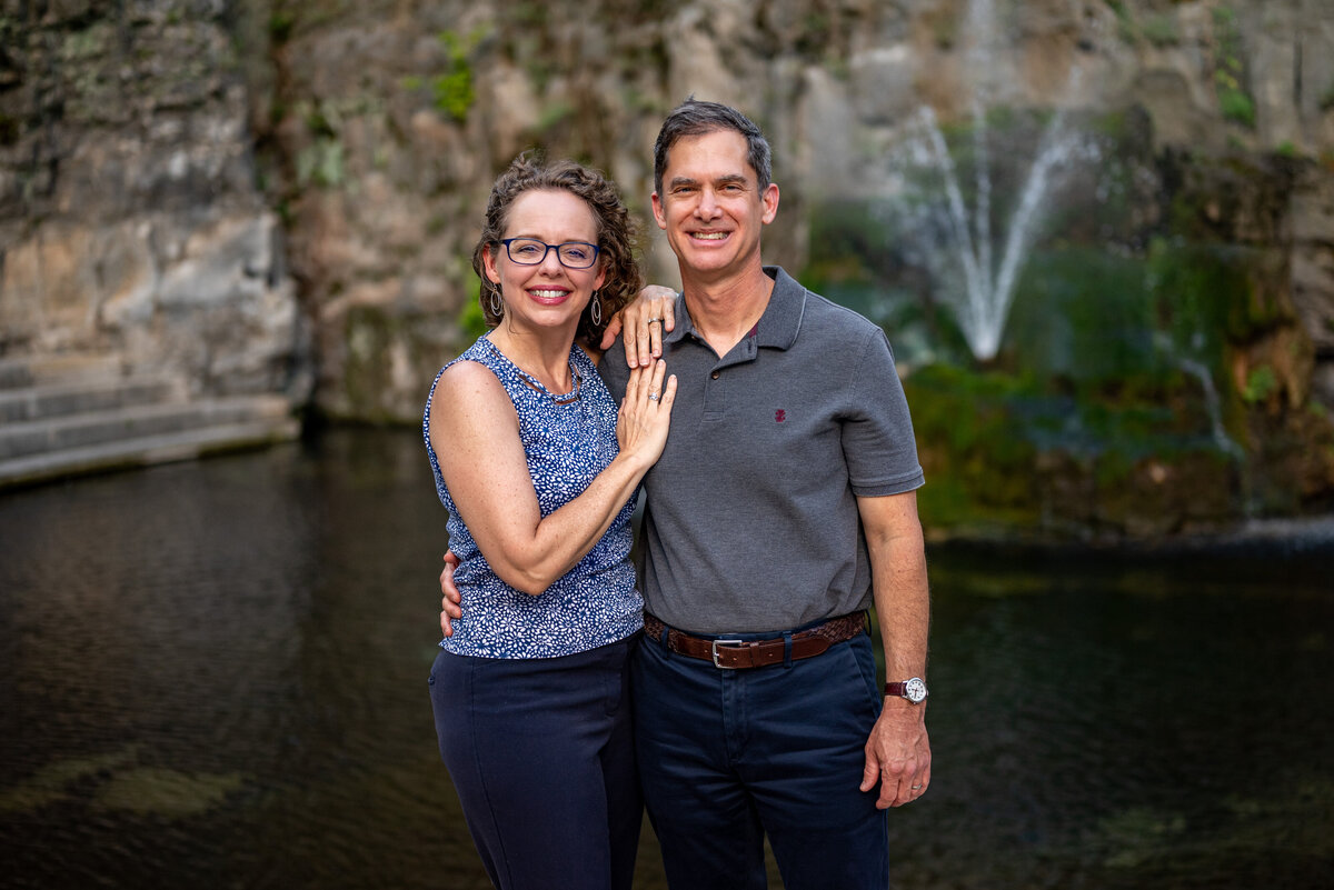 A husband and wife pose for family pictures in front of a fountain  in downtown Huntsville in Alabama