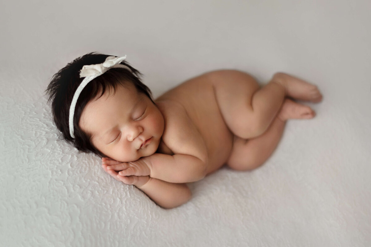 Newborn baby in a newborn photography photo session laying on a white backdrop with a bow in her hair in a northern virginia studio