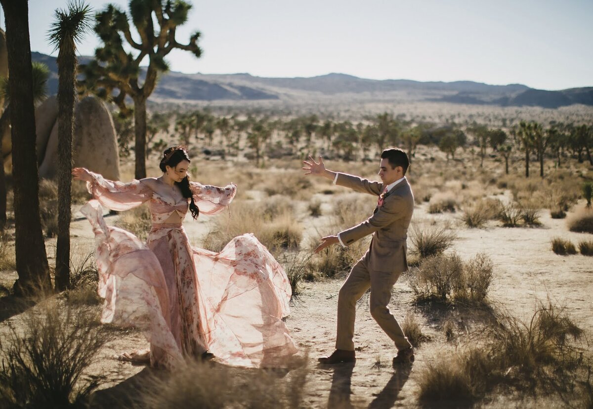 Grooms showing off his new wife as she twirls in a pink wedding dress in front of a Joshua Tree!