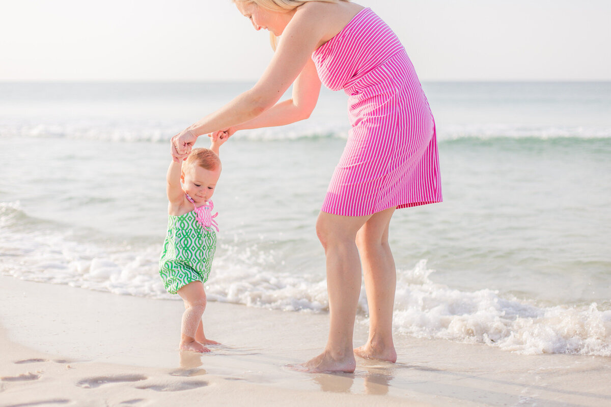 mom-and-baby-daughter-walking-at-edge-of-water