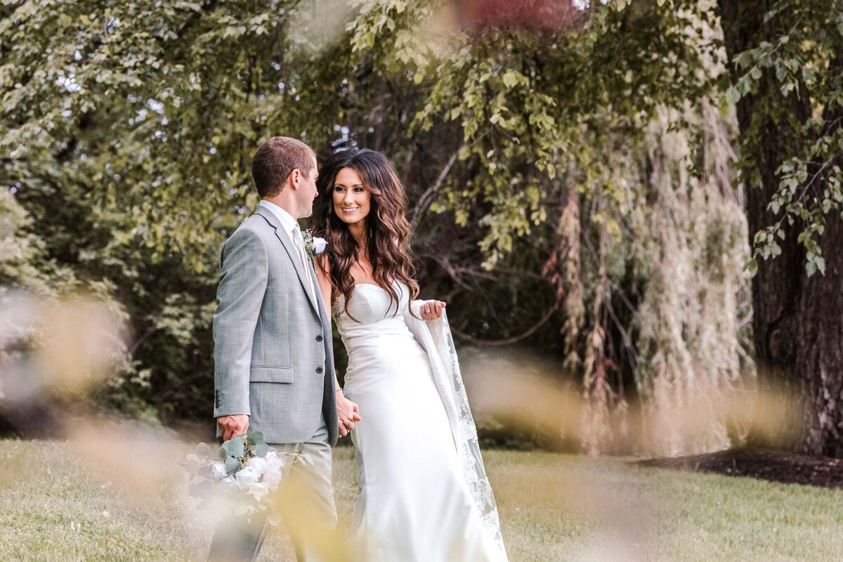 Bride and groom walk together hand in hand surrounded by trees with Spanish moss