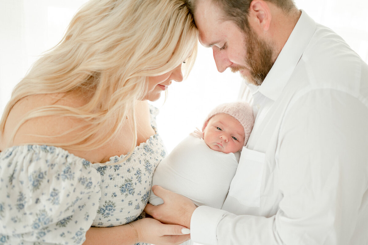 baby in a pink bonnet is held by her parents In Kristie Lloyd’s Nashville newborn photographer studio