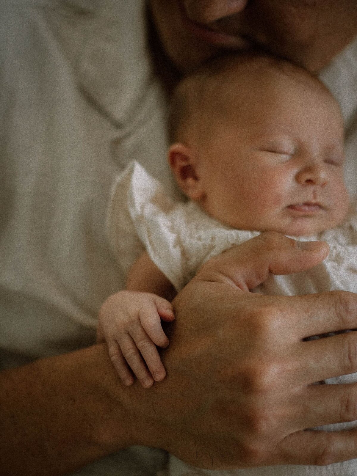 Close-up of a newborn sleeping peacefully in dad’s arms, tiny hand resting gently on his father’s hand during an in-home lifestyle newborn session in Temecula.