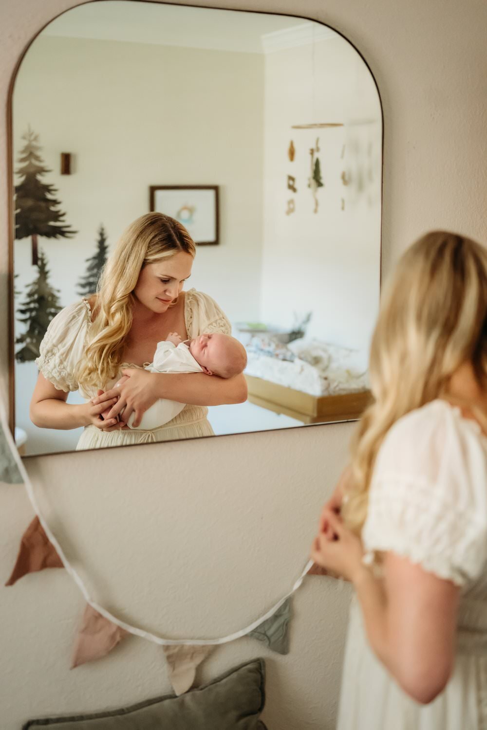 mom seen through nursery room mirror looking at her newborn son