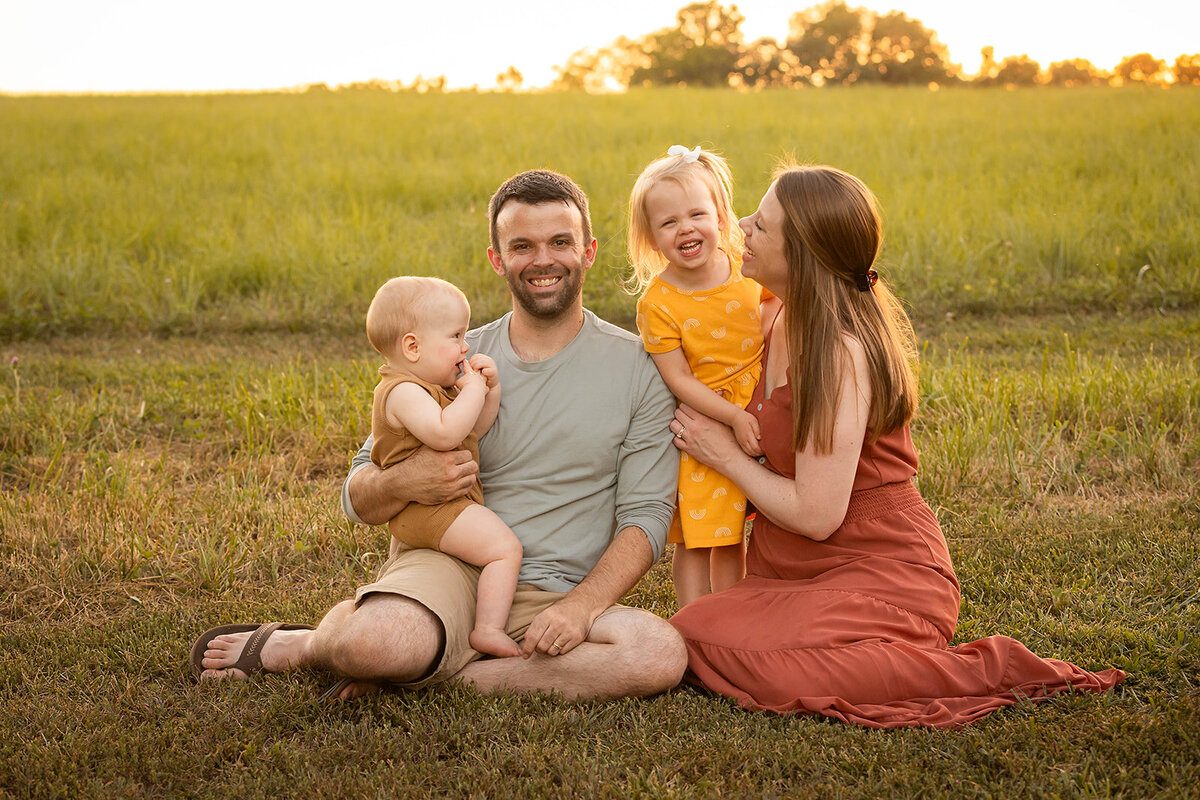 family of four laughing with field in background
