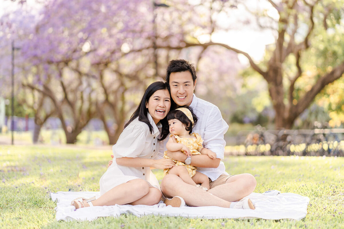 family of three sitting on picnic mat in sunset light with spring blossoms