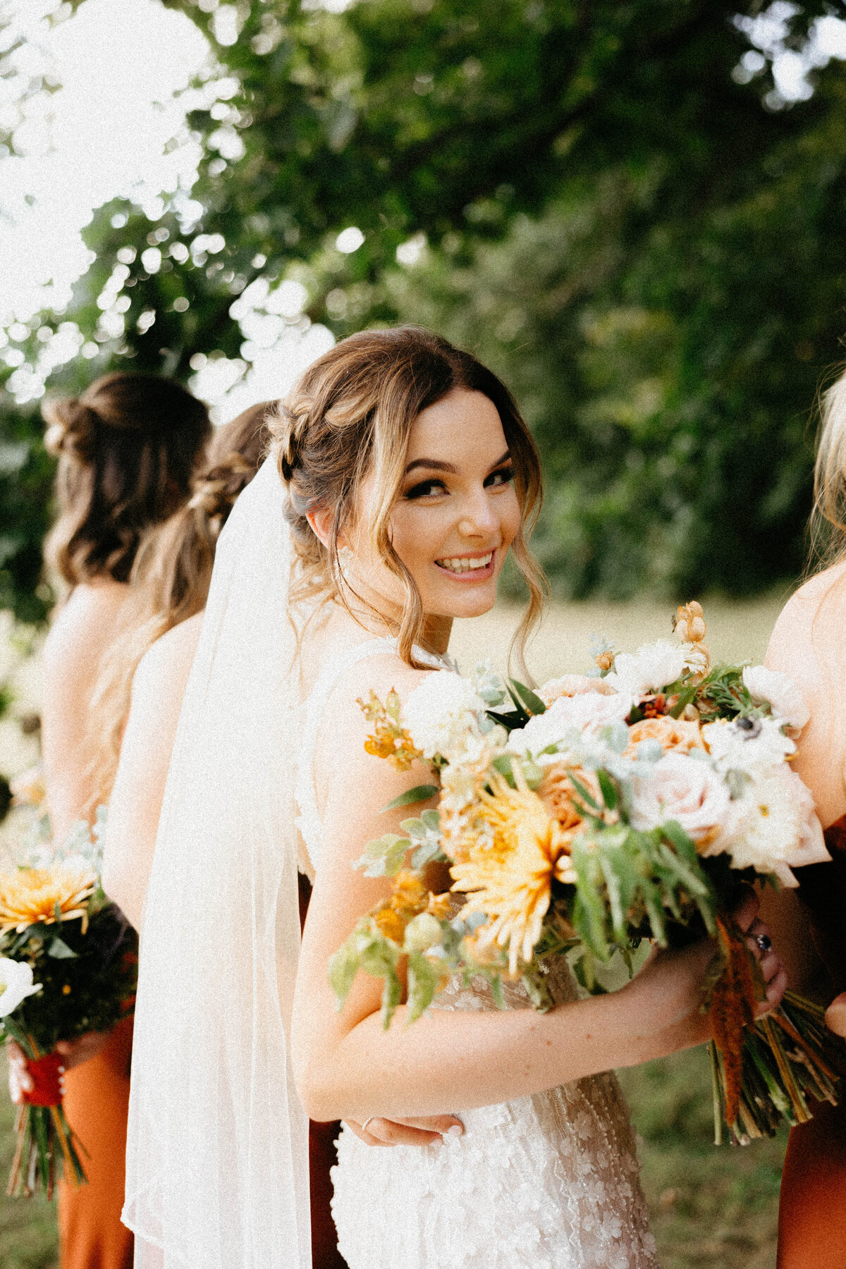 Bride holding bouquet with bridesmaids smiling at camera