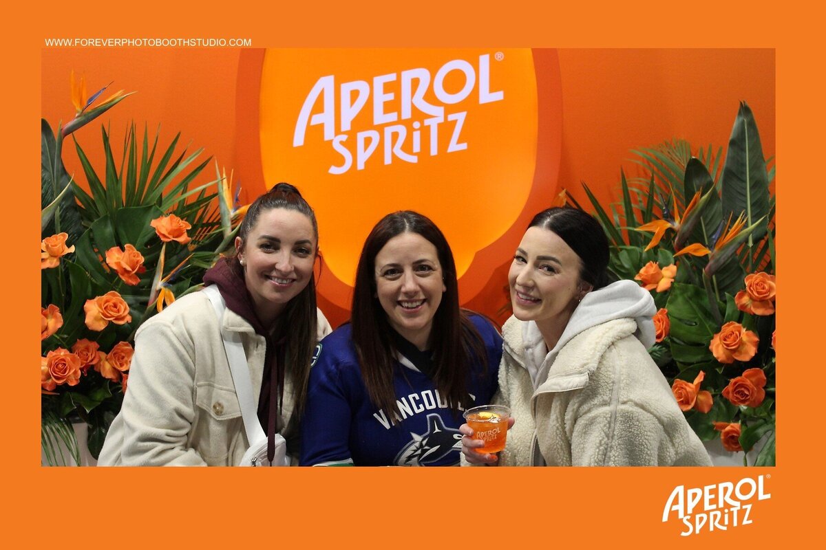 Co-workers in front of aperol spritz photo booth backdrop