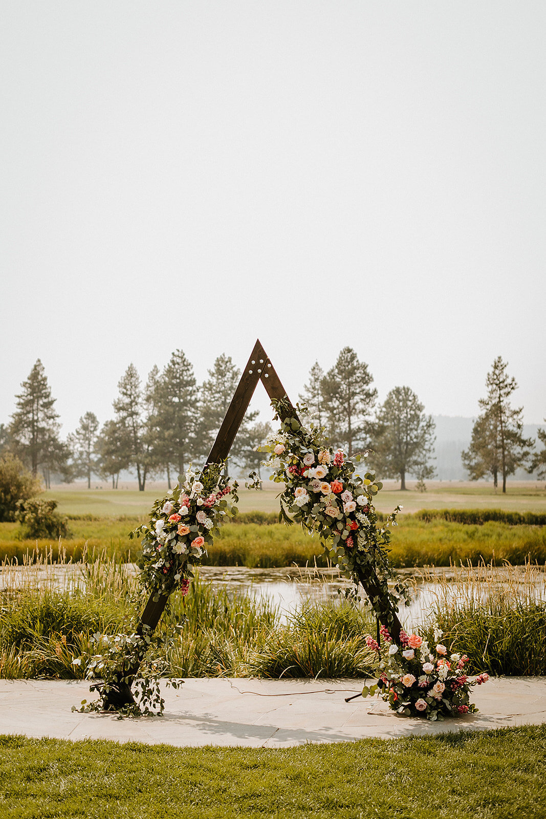 Triangle arch with peach, mauve and coral flowers and smilax vine at Sunriver Great Hall lawn