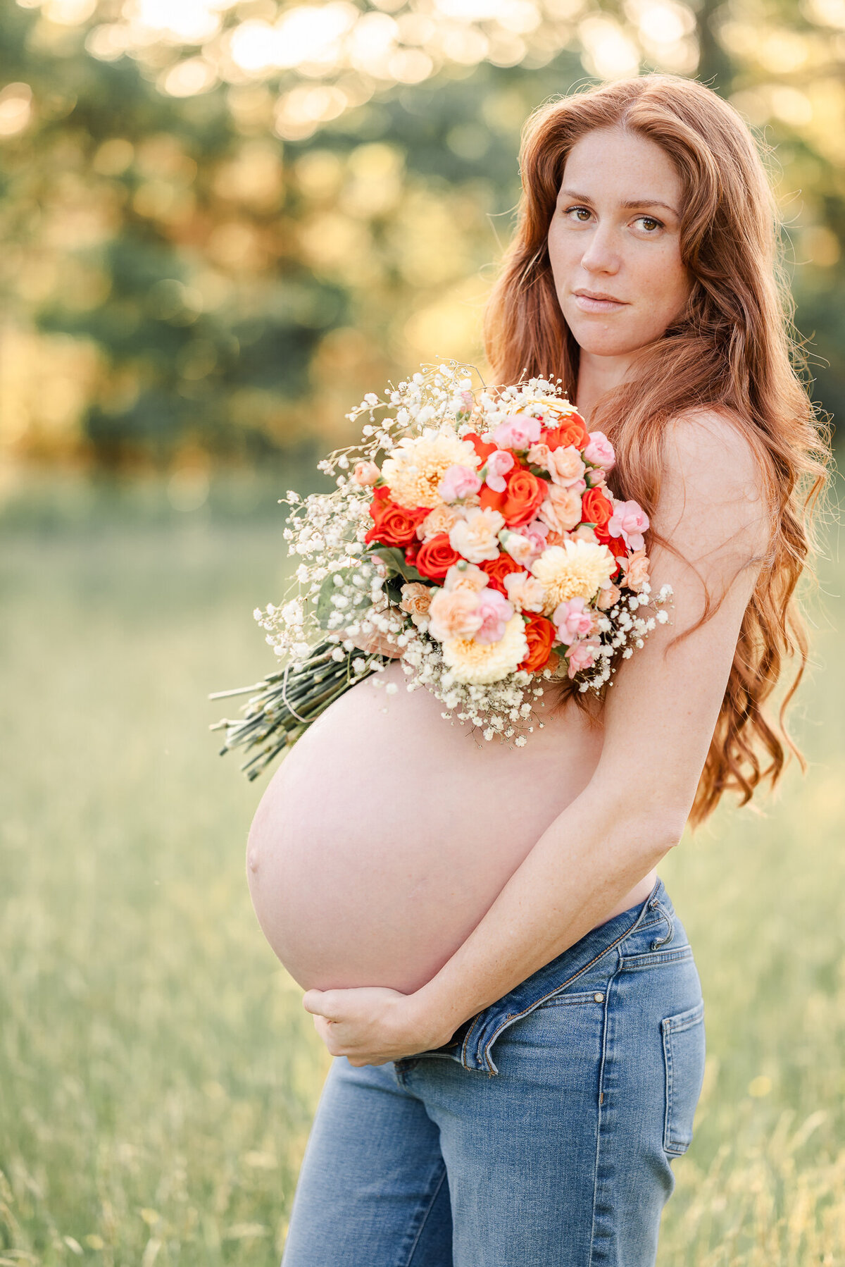 A mama-to-be wearing jeans, holds a  bouquet of flowers to create a top during her maternity session at Bells Mill Park in Chesapeake, VA.