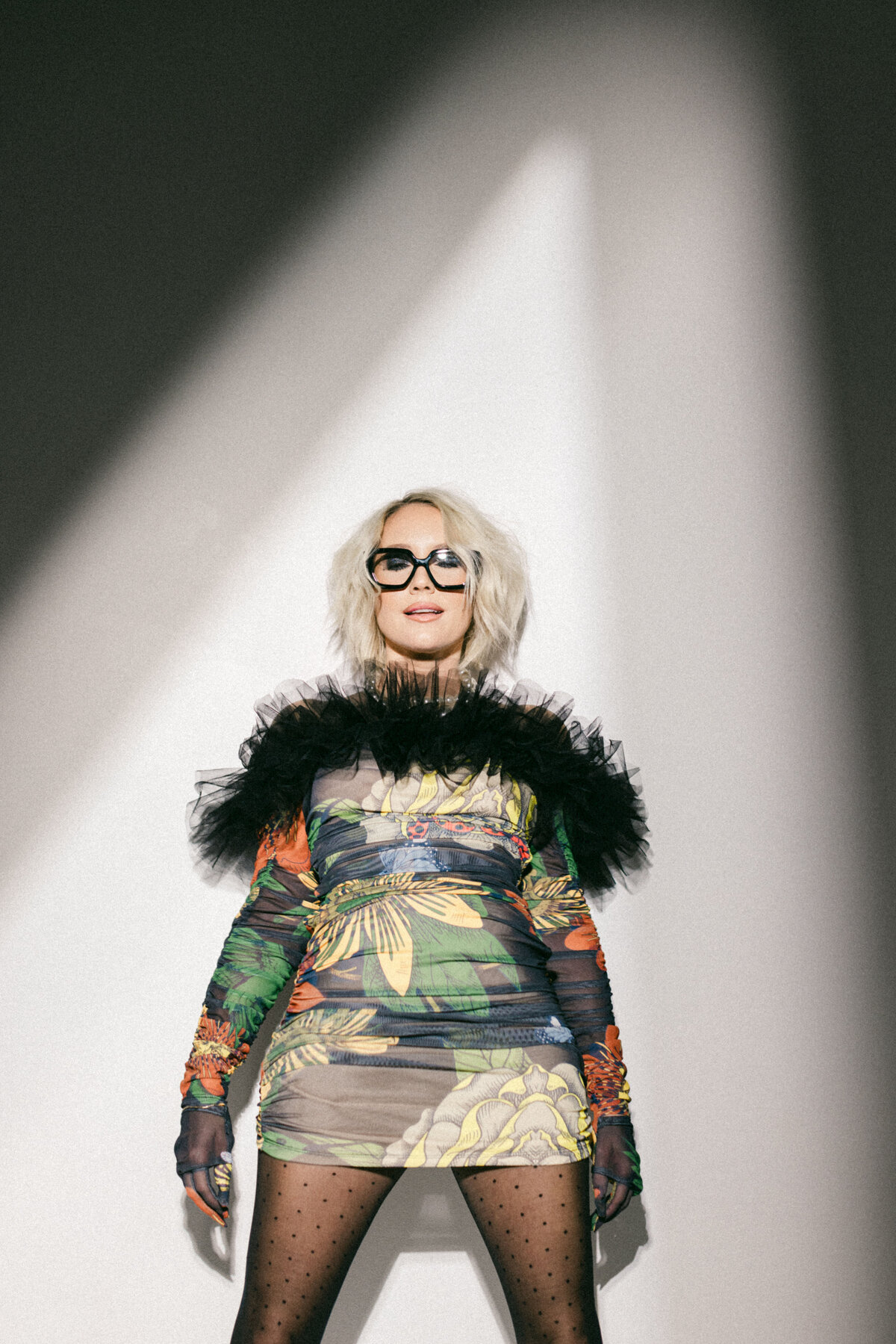 Stylized branding portrait of a woman in a floral mesh dress with dramatic black ruffles, standing confidently under directional spotlight. Dani Lacey Photographs