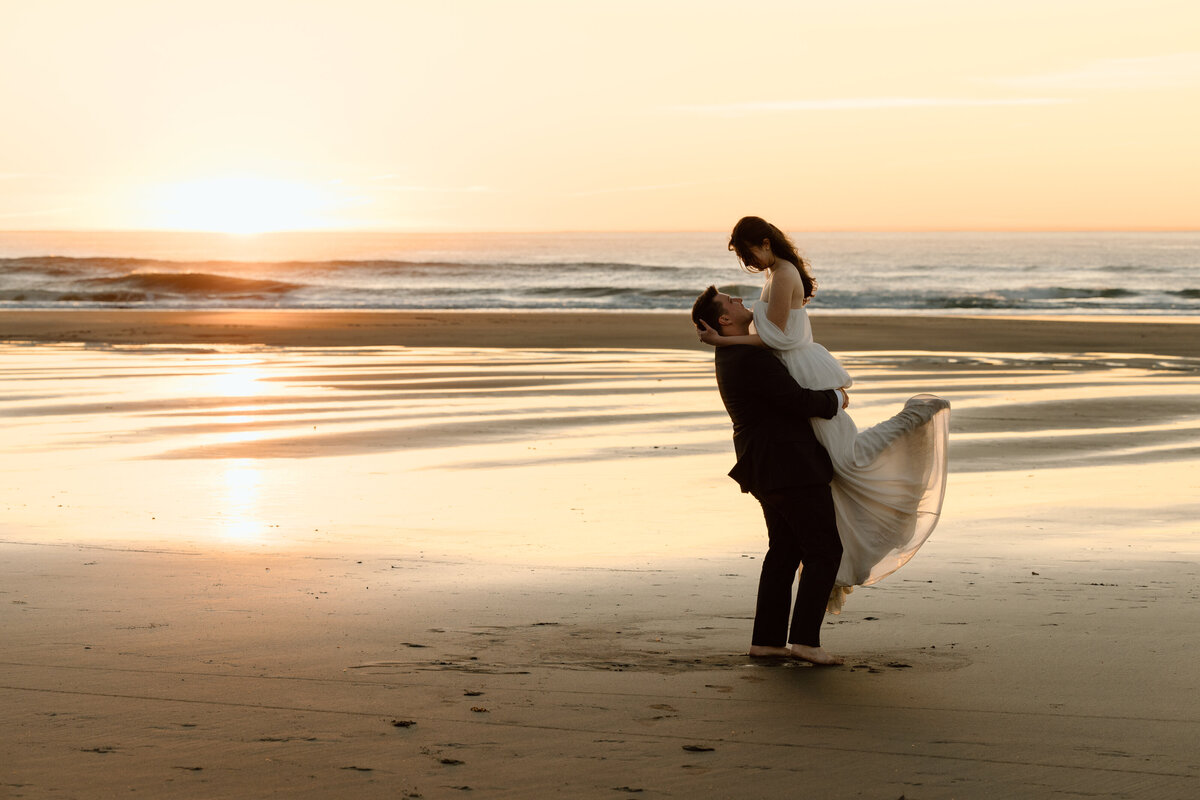 Groom spinning bride on the beach at sunset.
