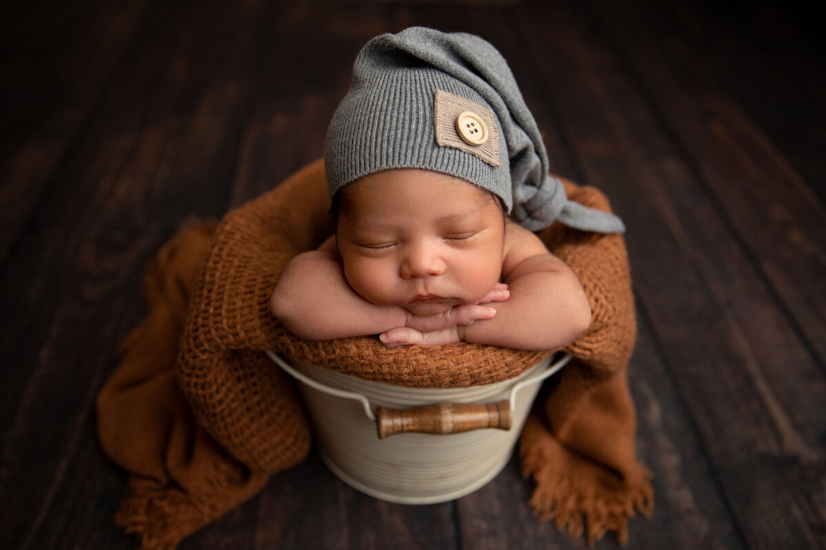 A peaceful portrait of a newborn baby sound asleep, nestled inside a cozy, rustic bucket. Soft blankets and neutral tones create a timeless and serene aesthetic, highlighting the innocence of your little one. Captured at Little Legacies Studio in Phoenix, Arizona, this image showcases our expertise in creating heartwarming newborn photography. Perfect for parents looking to preserve these fleeting moments with professional, artistic portraits.