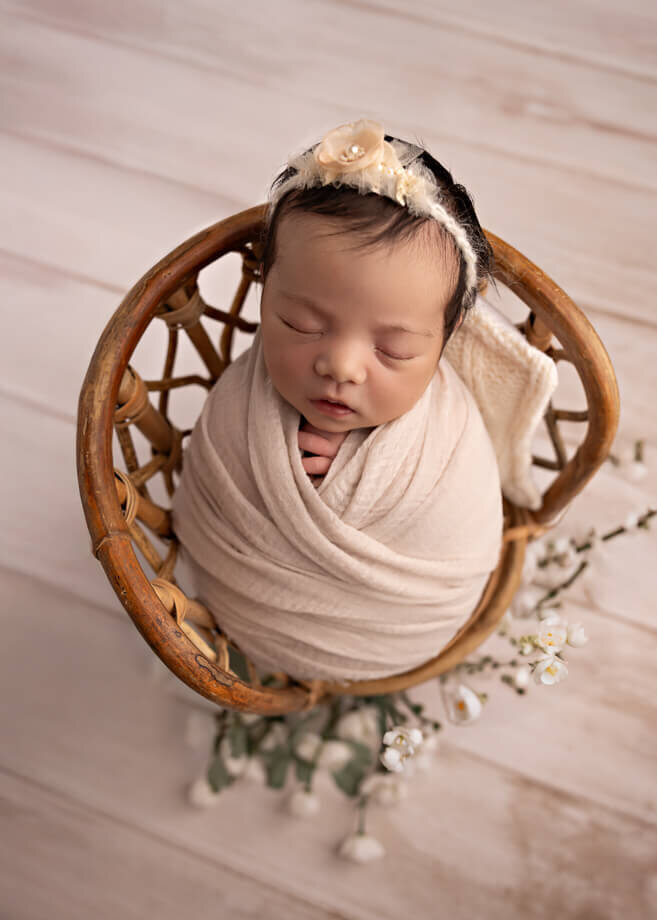 baby posed in a potato sac on a wicker chair decorated with white florals