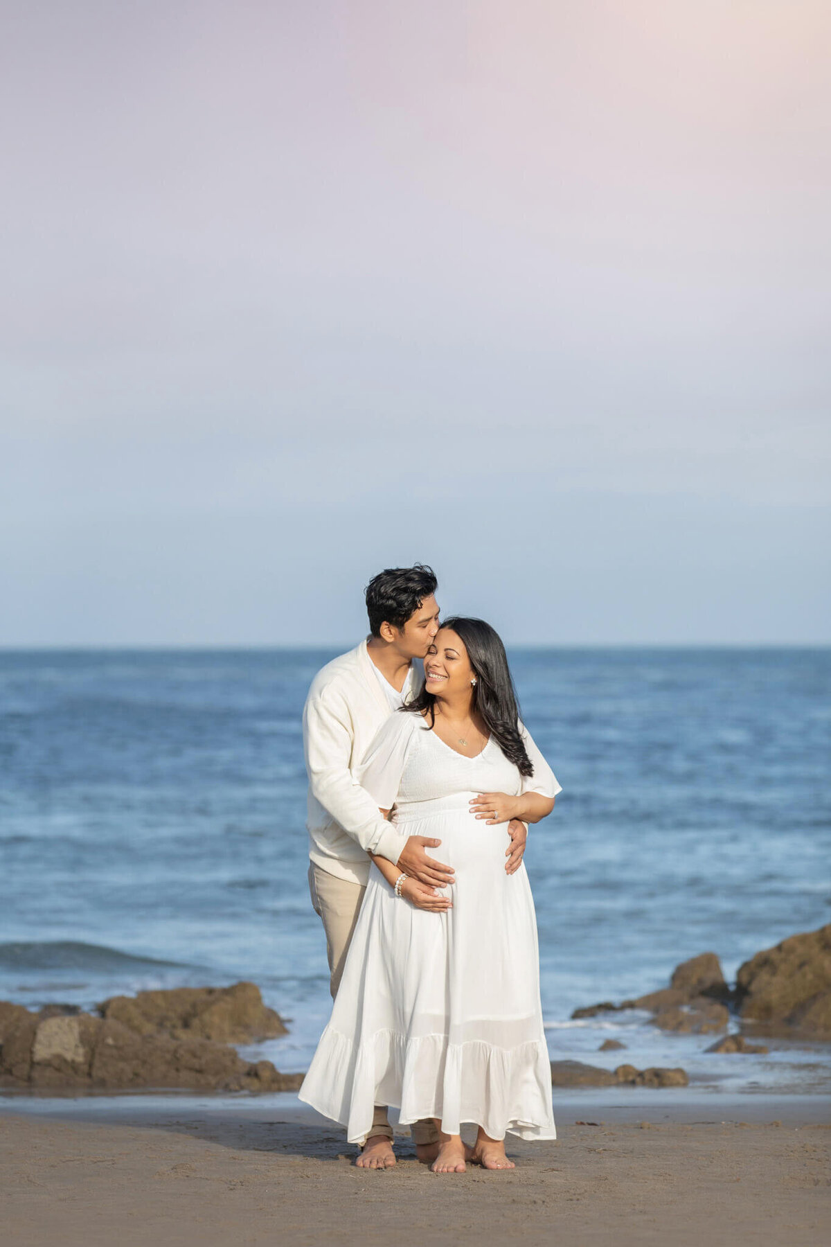 New mom and dad at Leo Carillo beach in Malibu at maternity photoshoot, dad kissing mom on the head, image by Los Angeles Maternity Photographer