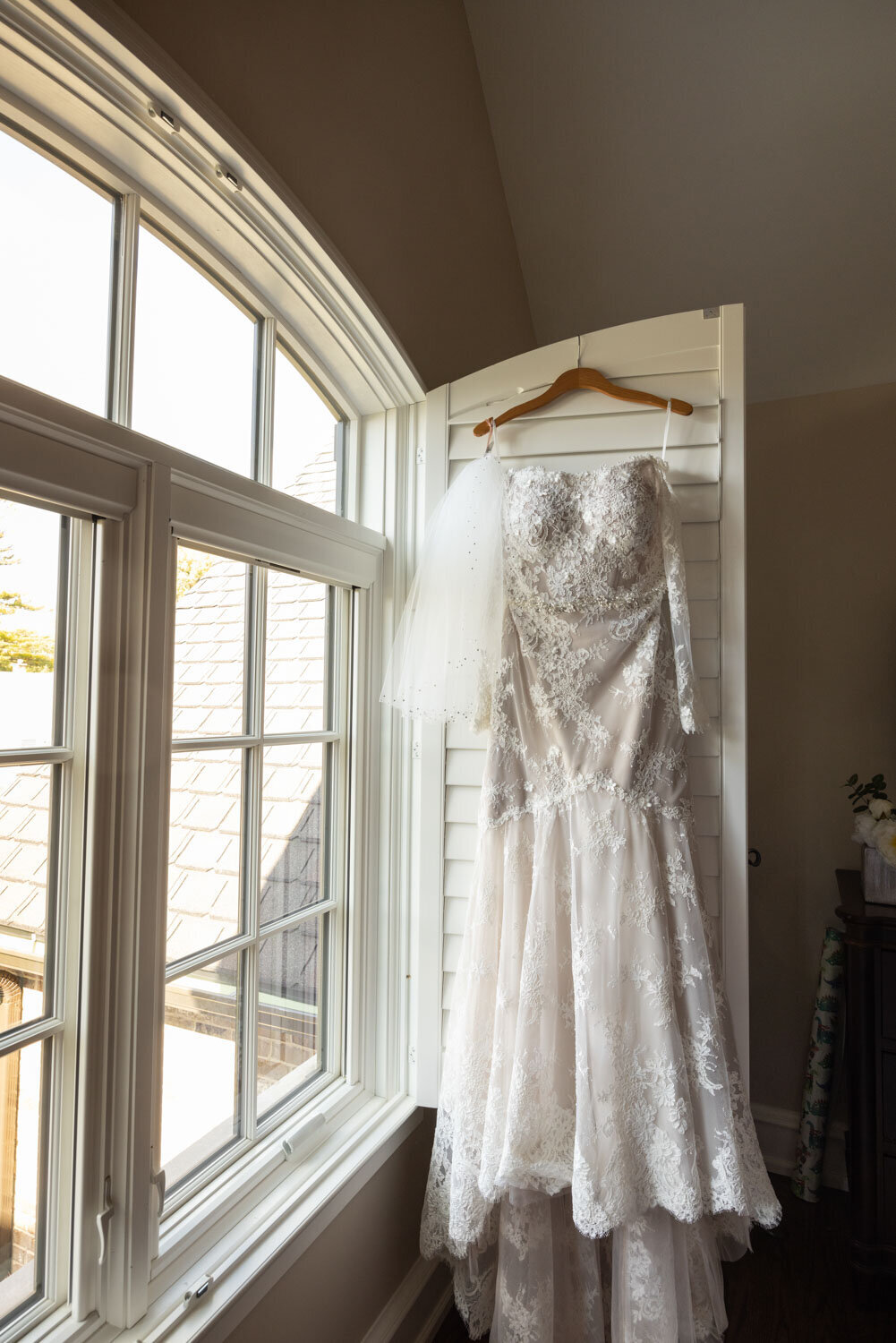 A wedding dress is hanging in front of a window