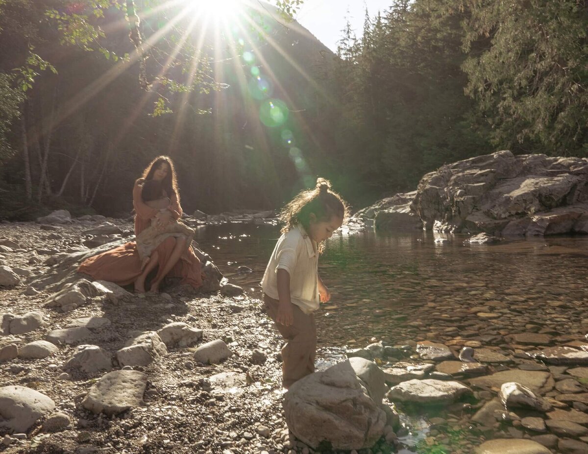 mother sitting on rock cradling daughter at creek with son