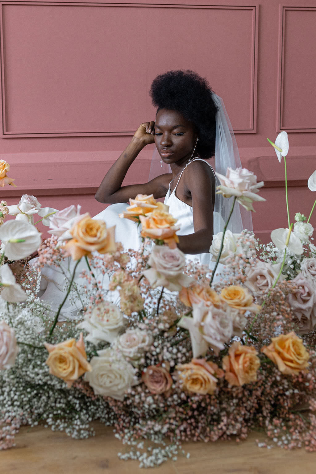 bride crouched down behind floral display
