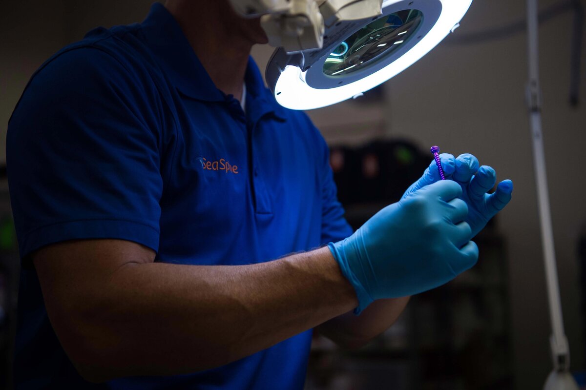 An employee at Seaspine used a magnifying glass and light to inspect a pedicle screw at production facility