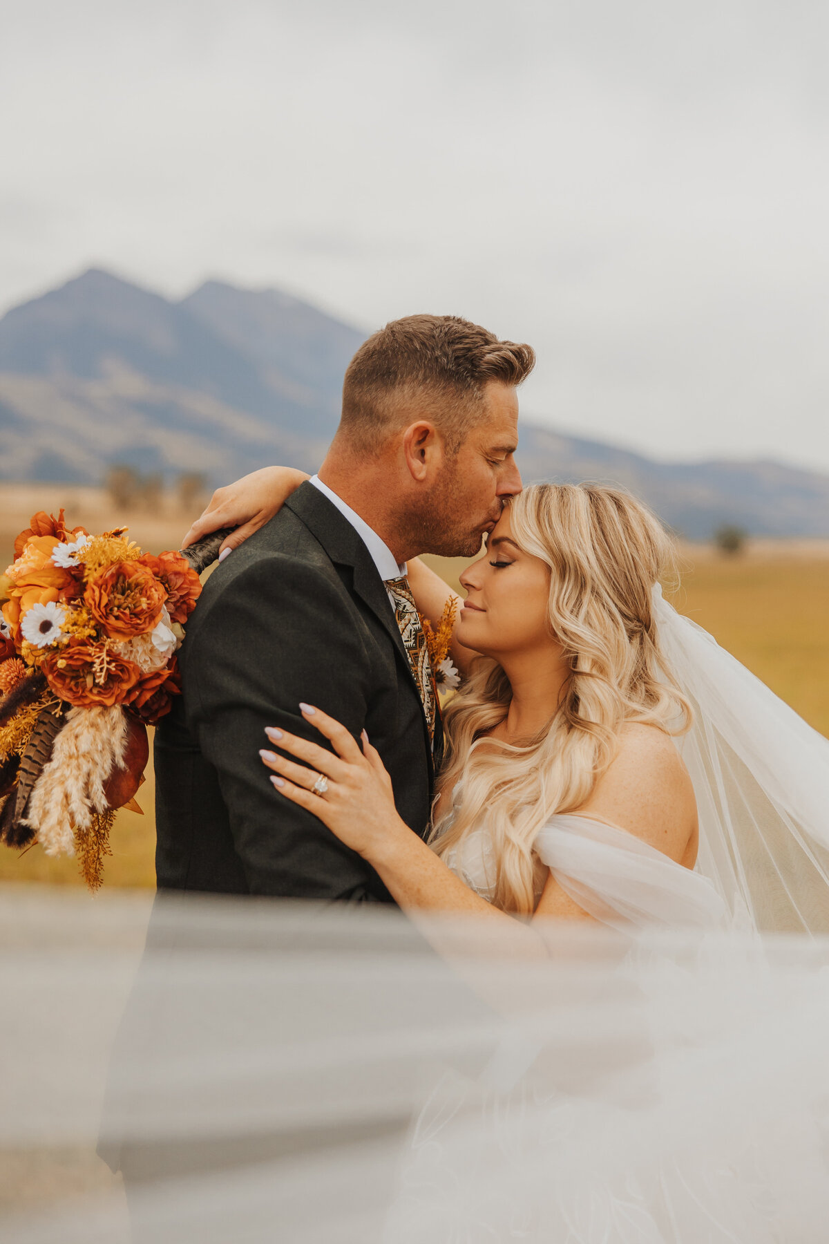 Groom gently kissing bride’s forehead during a quiet wedding moment.