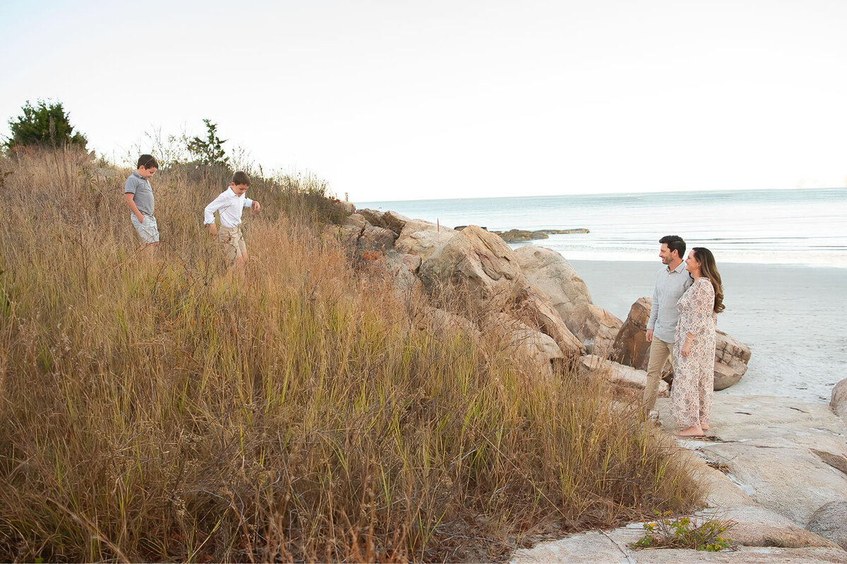 Two boys run down a grassy bank at Wingaersheek Beach to their parents who are waiting at the bottom.