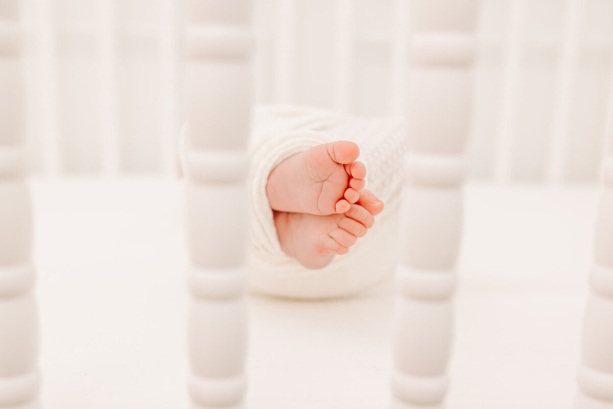 Newborn baby toes wrapped in white cloth and laying in her crib.