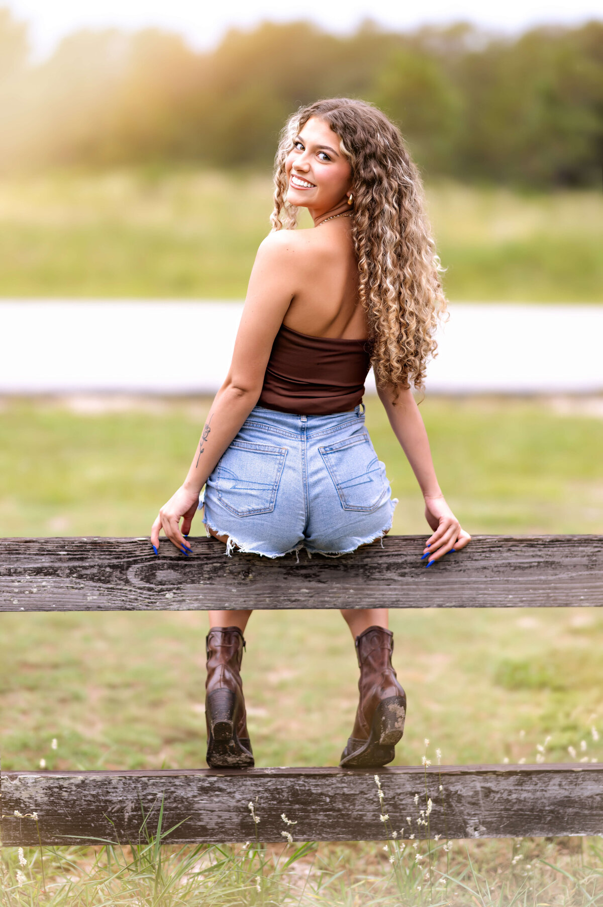 Golden hour senior portraits in Winter Garden with a girl smiling on a fence in dreamy sunlight looking back.