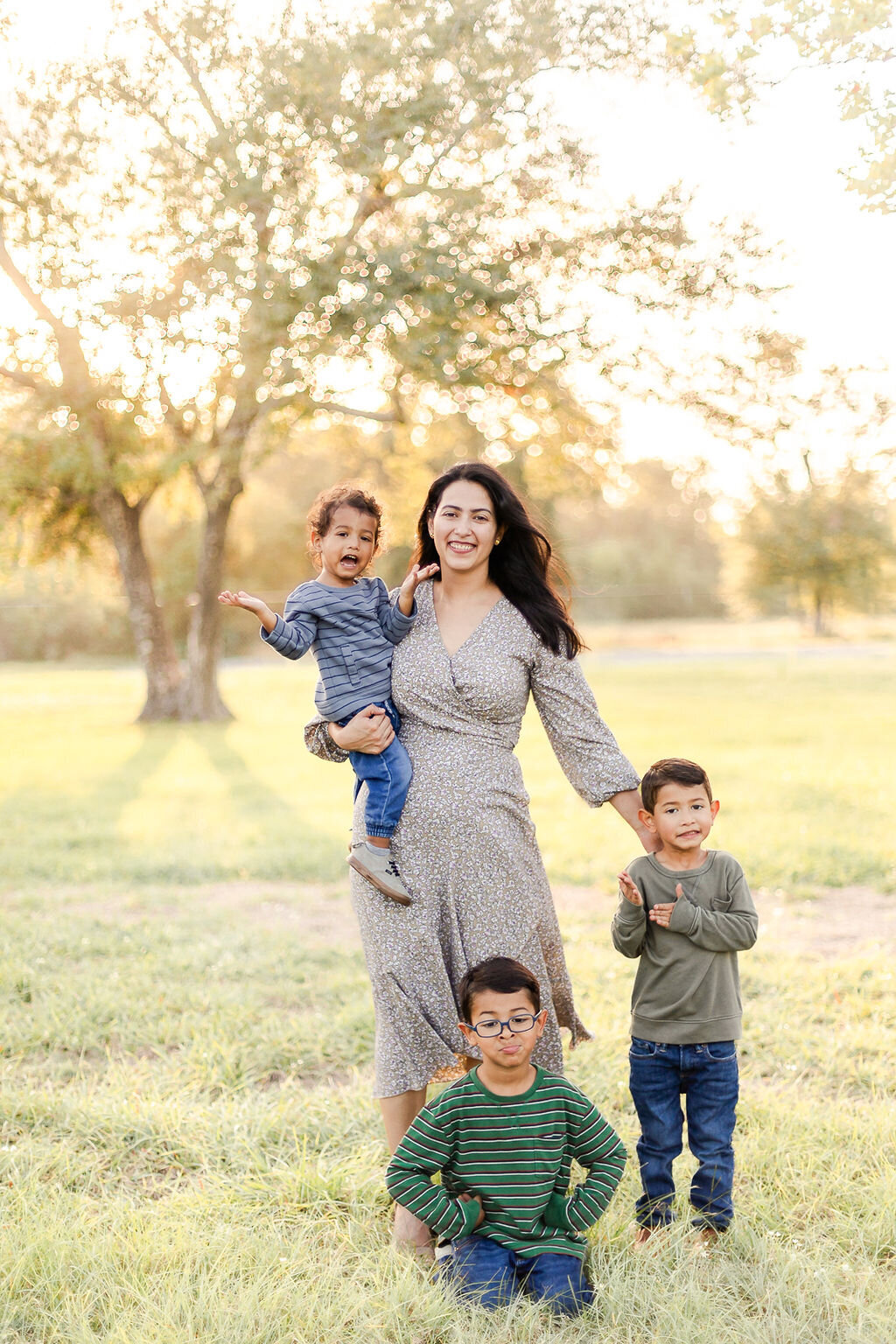 family portrait session at old town spring in Spring, Texas with the mother in floral, flowy dress while holding son in one arm and two other sons at her side
