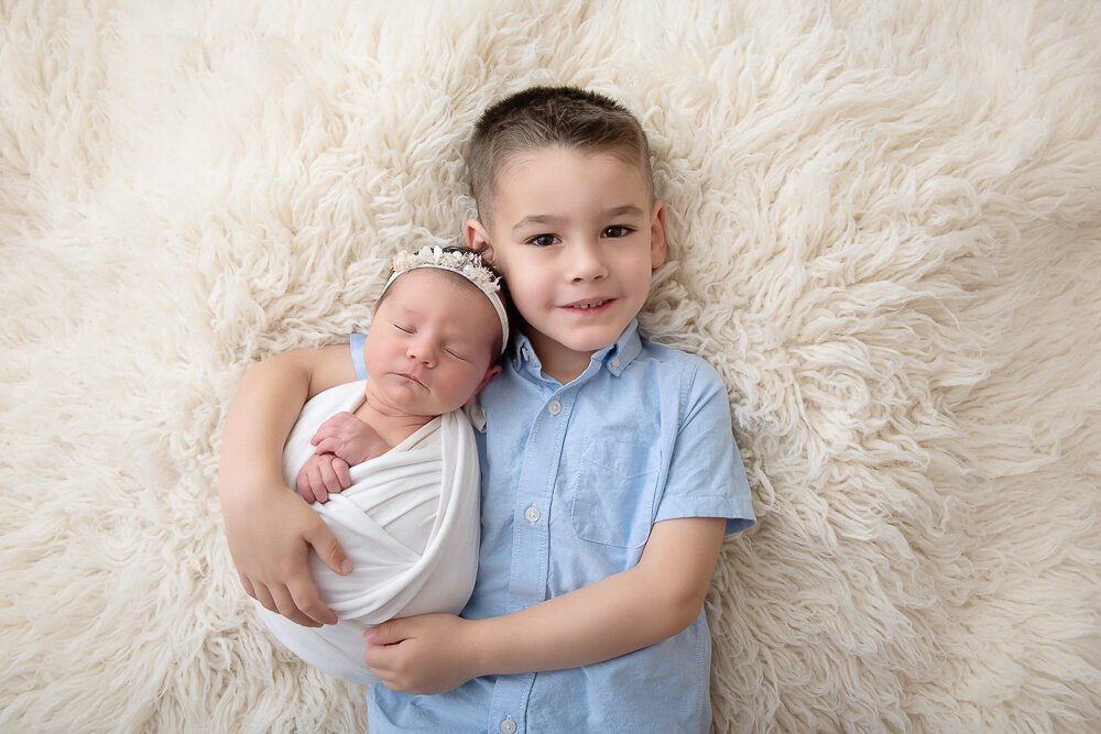 Big brother holding his baby sister on a cream rug for his Hamilton newborn photography session.