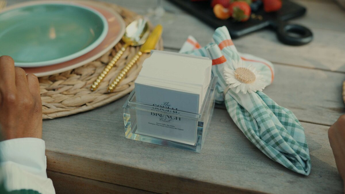 a close up of a table with plates and a stack of printed cards that say the social brunch club.