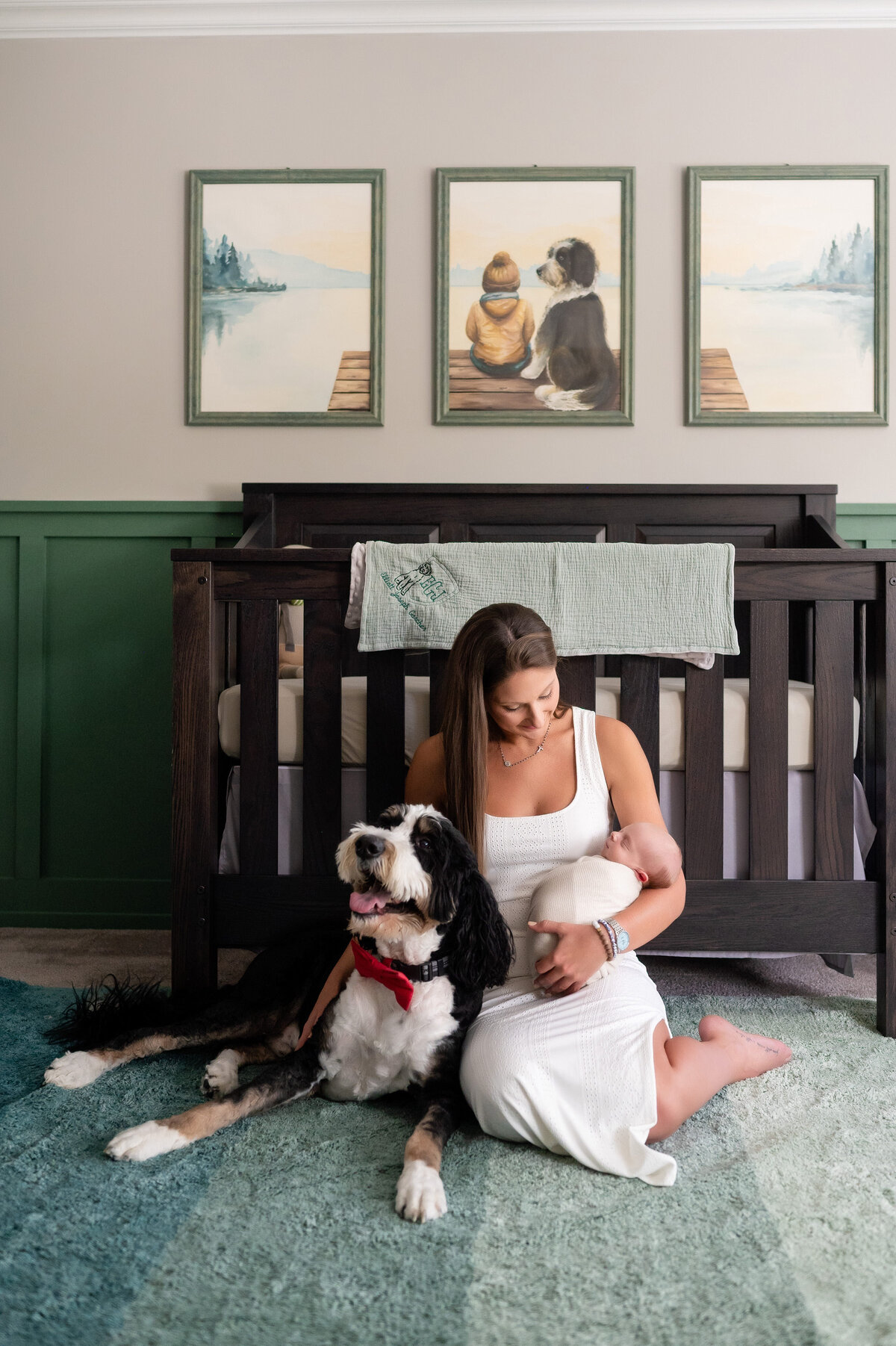 mom sitting with dog and baby in newborn baby nursery