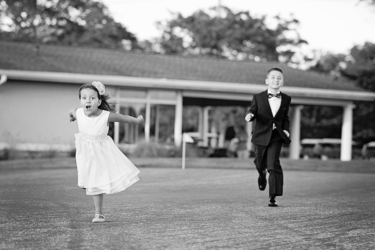 black and white photo of flower girl and ring bearer running outside wedding at Lawrence Yacht and Country Club