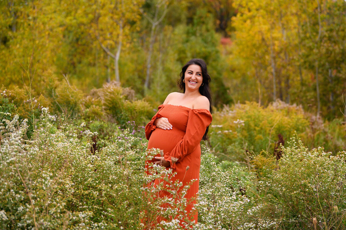 brown-haired woman wearing an orange maternity dress for her Burlington, On outdoor Fall maternity photography session