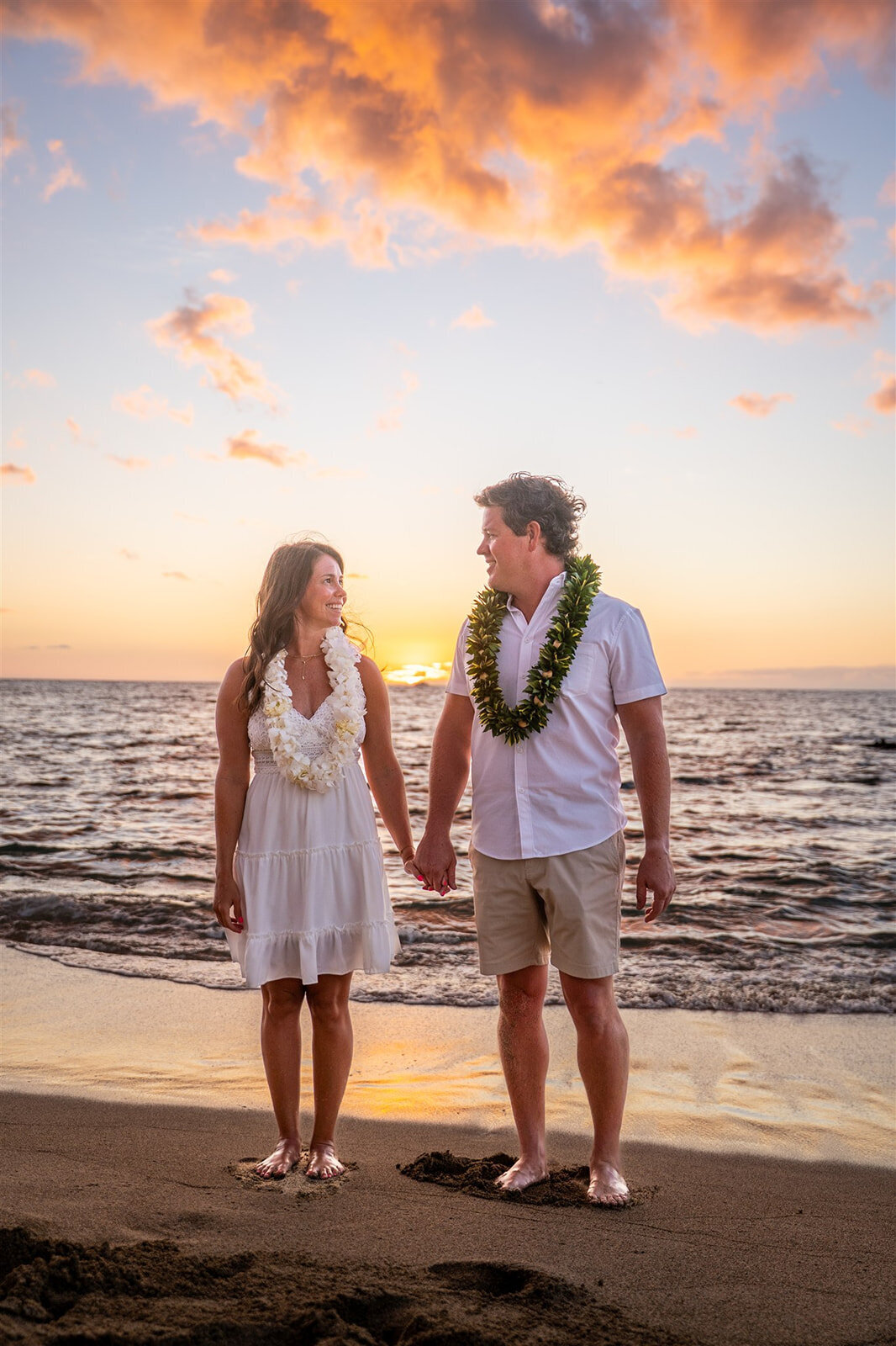 Couple wearing leis in the sunset and holding hands for Hawaii engagement photography session