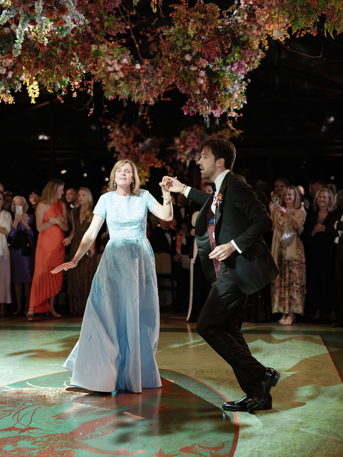 Interacting and sculptural floral clouds hang over the dance floor and bars of this fall wedding reception in Tennessee. Clear top tent build out for fall wedding reception in Tennessee hills.  Product clustered floral clouds in a tasteful fall color palette of copper, ruby, gold, burgundy, rust, and lavender. Orchids, bittersweet berries, butterfly ranunculus, and tulips are highlighted. Unique floral design with flower forward large scale installations. Design by Rosemary & Finch Floral Design in Nashville, TN.