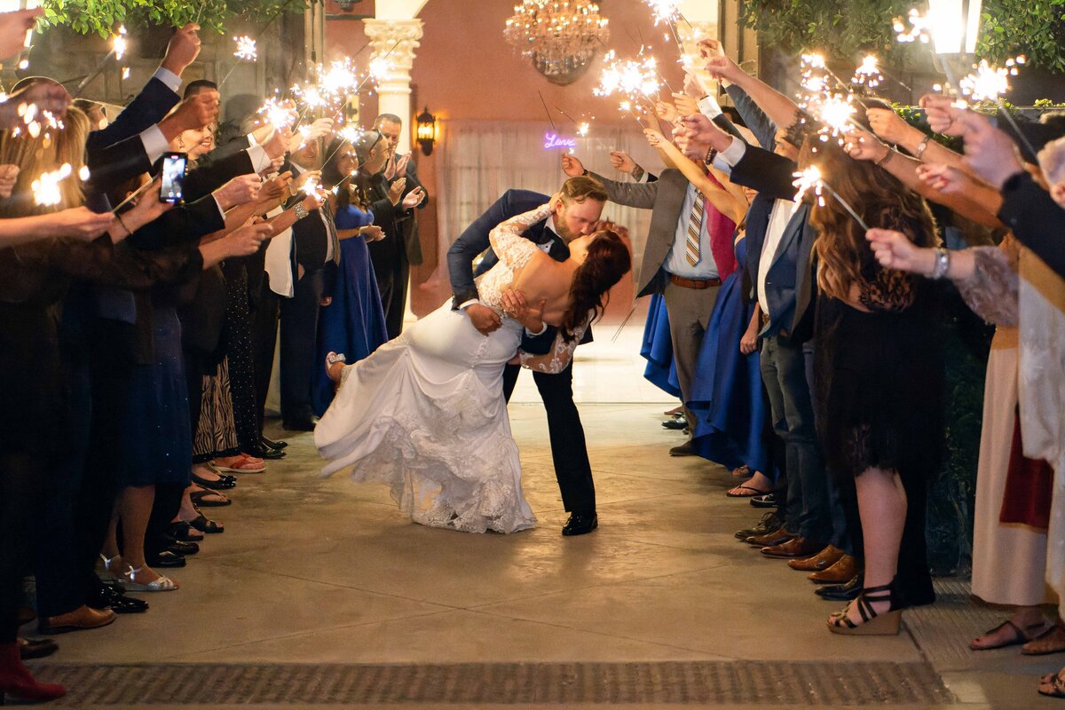 Groom dips his bride for a kiss as they make their wedding exit through sparkler send off