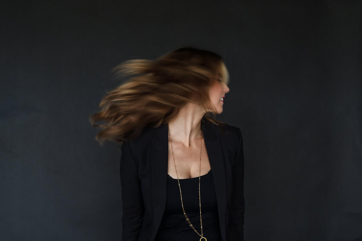 Woman in black blazer turning head with hair flowing during indoor brand photoshoot
