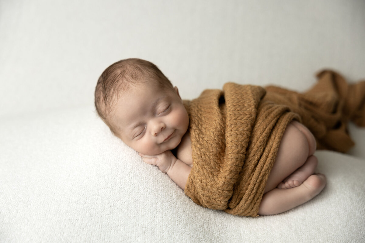 A newborn cuddles in a brown blanket in this St. Louis newborn studio