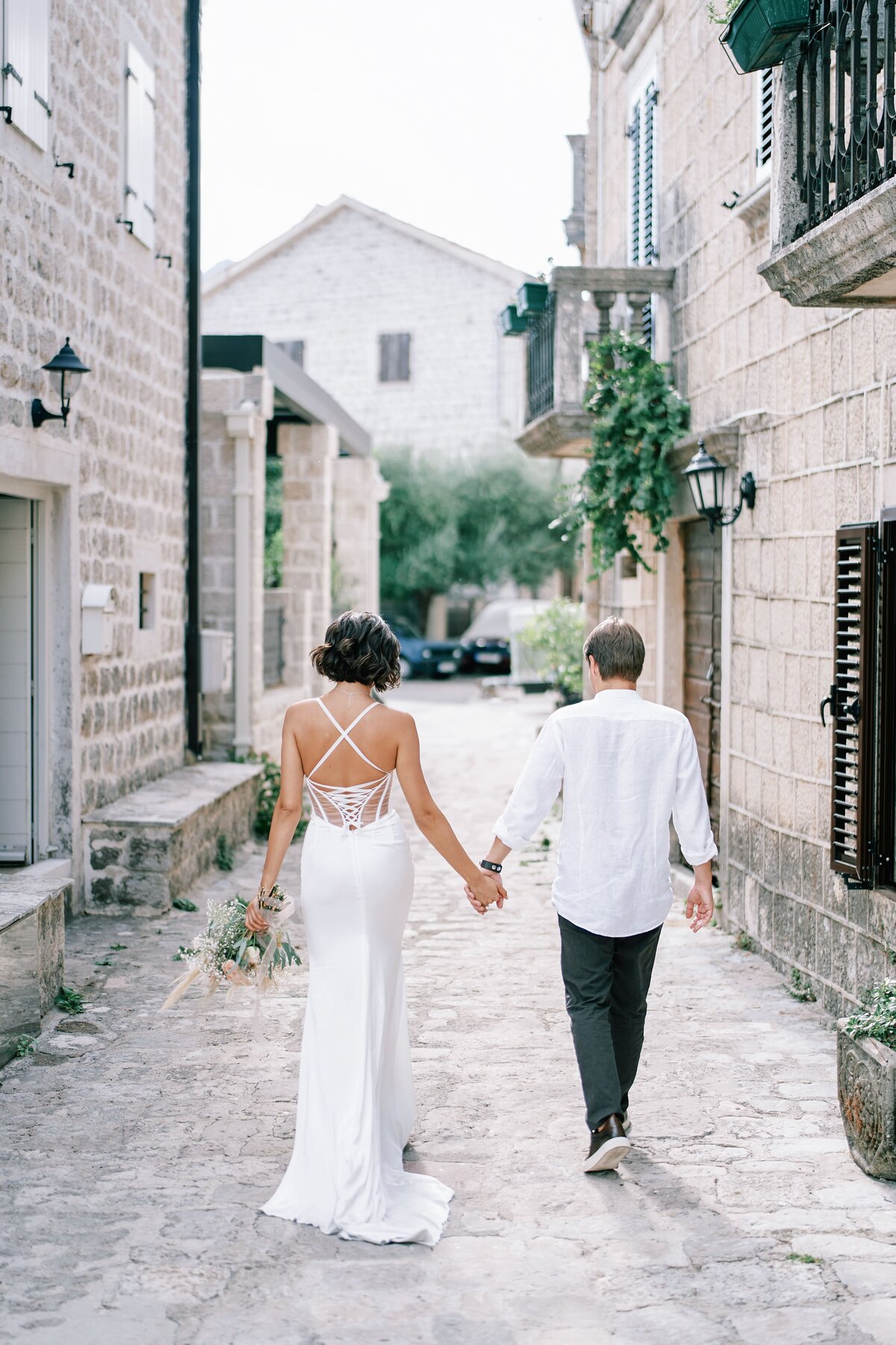 bride-groom-are-walking-holding-hands-along-narrow-street-ancient-town-back-view
