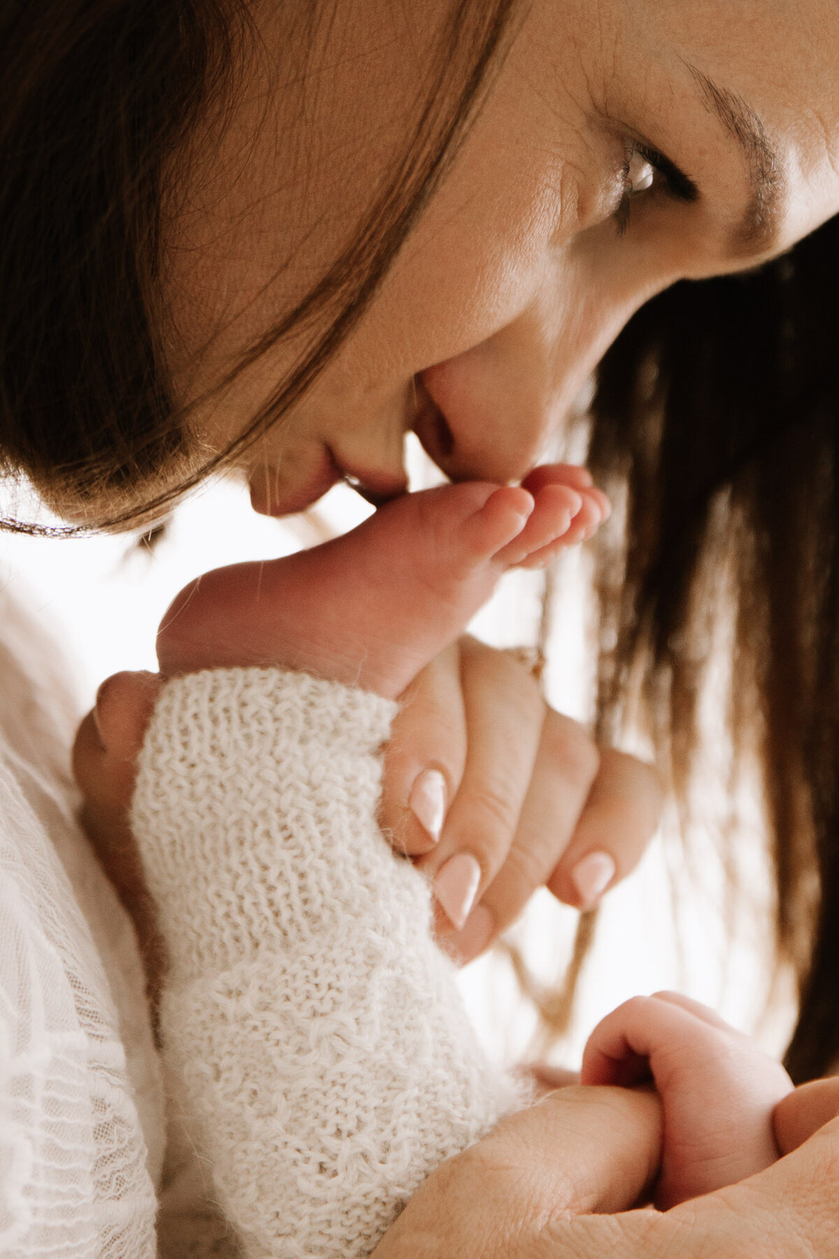 Close-up of a mother gently kissing her newborn’s tiny foot during a tender moment, captured in a soft and natural light studio in Southwest Sydney.