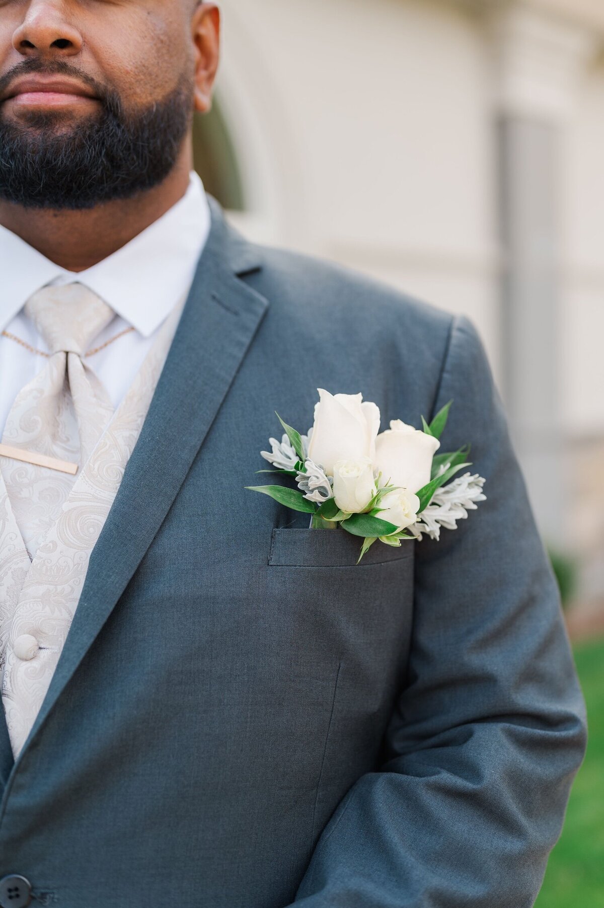 Two white garden roses peek out of a front pocket of a groom's suit
