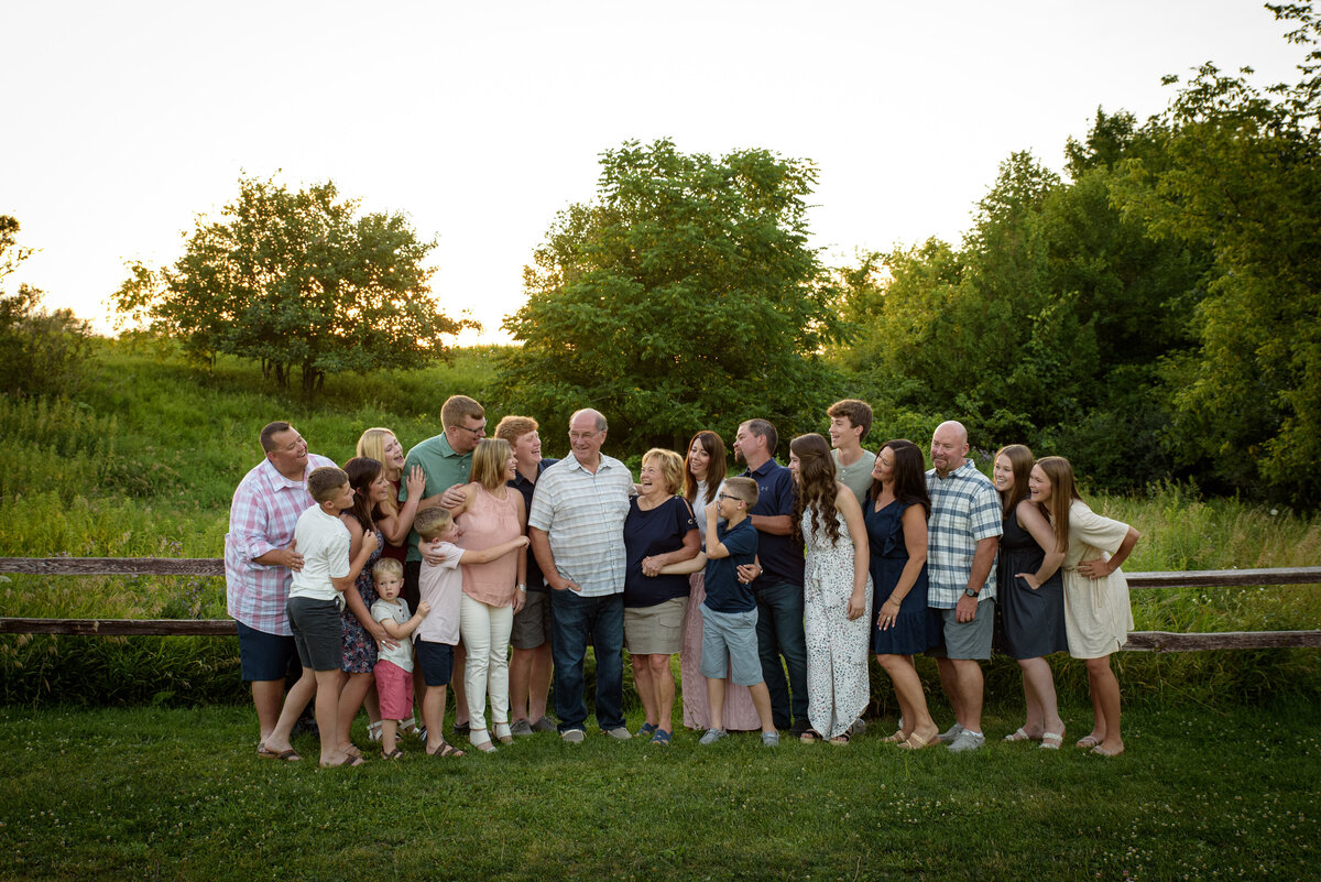 Large extended family portrait with family standing in long grassy area at Fonferek Glen County Park near Green Bay, Wisconsin with fence and sunset in background