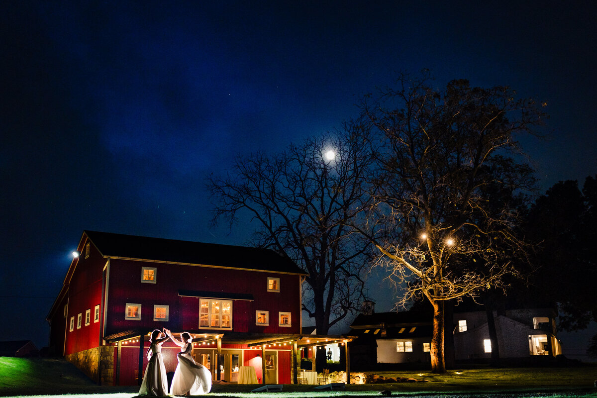 A wedding couple dancing in the field at night in front of the red barn at Cornman Farms in Dexter Michigan