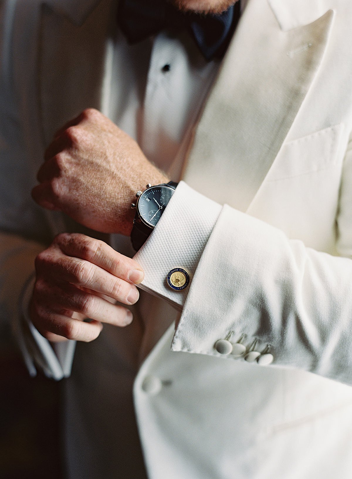 The groom getting ready by putting on his cufflinks and his white tuxedo jacket before the wedding.