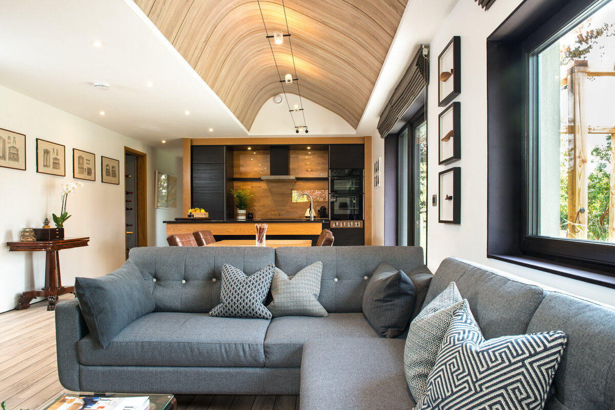 Bright open plan living and kitchen area with greay sofa and curved wood ceiling feature